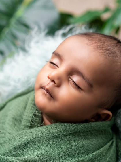 Nestled in nature's embrace. This newborn is wrapped in a beautiful shade of green, surrounded by lush leaves for a fresh, organic, and calming portrait.