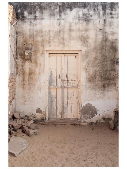 A weathered door on a decaying wall in a sandy courtyard in Rajasthan. This minimalist shot captures the beauty in texture, decay, and the stories old buildings tell.