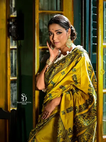 Actress Sohini Sarkar in a vibrant yellow saree for a Sangbad Pratidin Pujo shoot. The warm, indoor lighting and her playful pose create a festive and joyful mood.