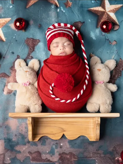 A sleepy little elf for Christmas. This adorable newborn is wrapped in red with a festive hat, ready for their first holiday season. The teddy bears add an extra touch of sweetness.