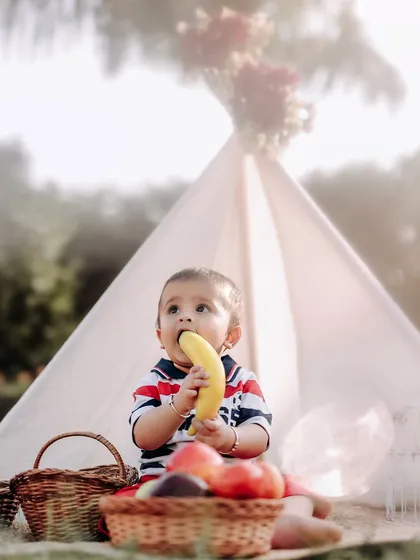 A healthy snack during a fun outdoor photoshoot. This little one is enjoying a banana at his picnic, a real and adorable moment captured on camera.