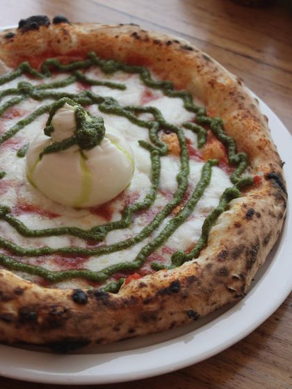 A close-up of our Burrata Pesto pizza. The whole burrata is the star, waiting to be broken open.