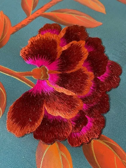 A close-up of the exquisite craftsmanship in our Folly design. The vibrant, multi-tonal embroidery of this flower showcases the artistry and detail that bring our wallcoverings to life with texture and color.