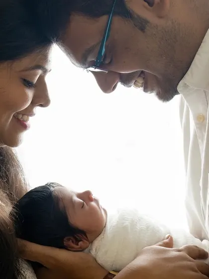 The first hello. This backlit newborn portrait captures the tender, intimate moment when new parents gaze at their baby, creating a soft, angelic memory of the beginning of their family story.