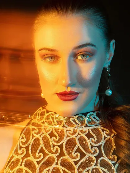 A close-up using split-colored lighting. The warm orange and cool blue light on either side of the face creates a striking, high-fashion look.