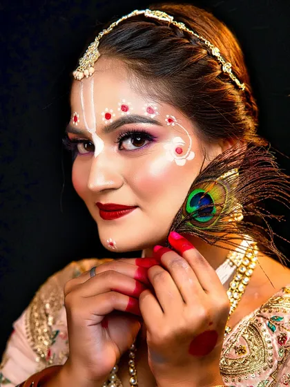 A close-up of the Radha makeup, with a peacock feather prop. The details, like the white floral patterns, showcase the student's precision.