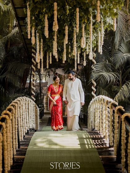 A couple walks hand-in-hand across a bridge decorated with hanging floral arrangements. This shot captures a serene moment during their South Indian wedding, symbolizing their journey forward together.