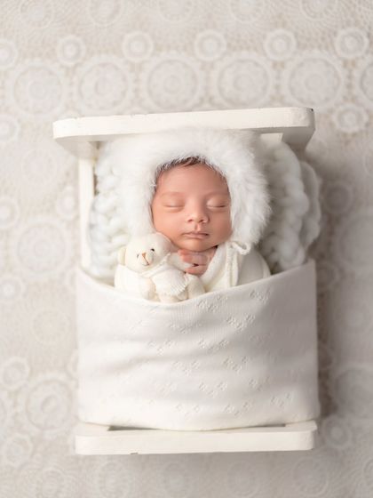 Like a little snow angel. This all-white setup with a fluffy-hooded outfit and tiny teddy bear creates a dreamy and pure newborn portrait.