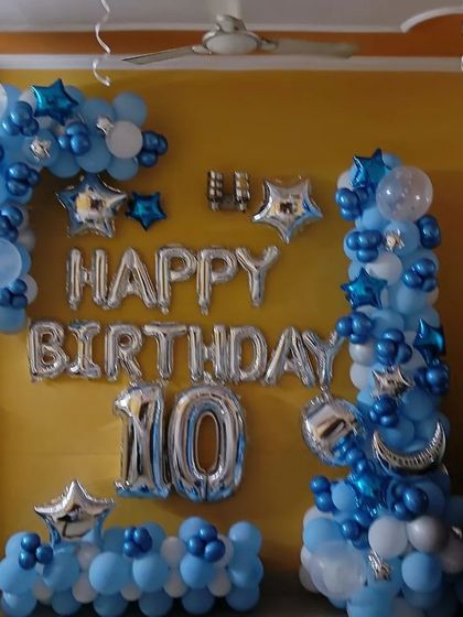 A blue and silver themed birthday decoration for a 10th birthday at home. The setup includes balloon pillars, 'Happy Birthday' foil letters, and star and moon-shaped foil balloons.