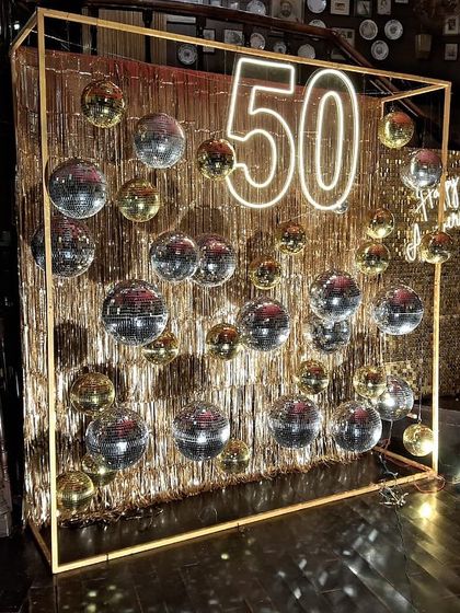 A closer look at the stunning 50th-anniversary decor. The combination of a neon '50', a gold fringe curtain, and hanging disco balls created a spectacular, glittering photo opportunity for the guests and the celebrating couple.