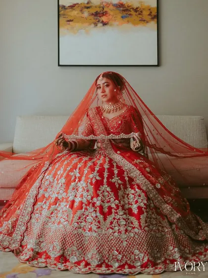 A classic bridal portrait. The bride, seated and draped in her magnificent red lehenga, looks every bit the part of a traditional, royal bride.