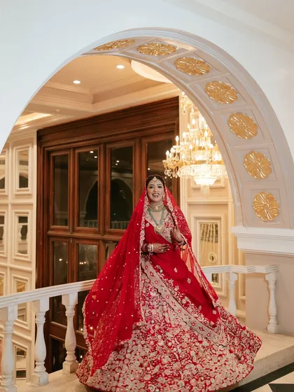 A full-length view of this magnificent bridal look. The grand setting and her stunning red lehenga called for makeup that was both classic and striking, ensuring she was the center of attention.