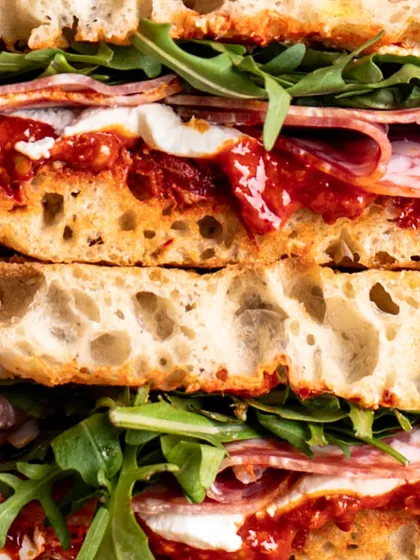 A macro close-up of a salami sandwich, where you can see every detail of the airy focaccia bread, fresh arugula, and cured meat.