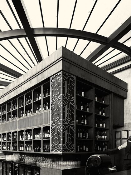 A detailed view of the custom art-deco style panel on the bar, a nod to Calcutta's architectural history. The fully stocked shelves add to the classic bar atmosphere.
