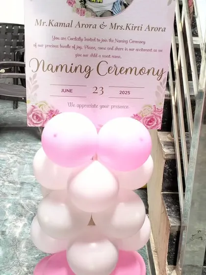 A close-up of a personalized welcome stand for a Naming Ceremony. It provides all the event details for guests and is decorated with a simple pink and white balloon pillar.