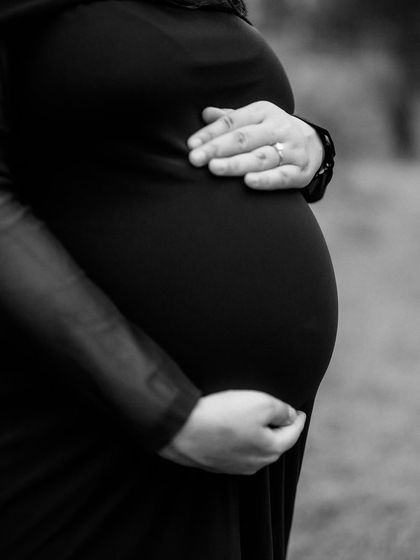 A close-up in black and white, focusing on the beautiful shape of the baby bump. The mom's hand resting on her belly adds a touch of tenderness.