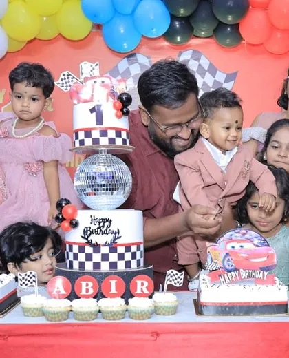 A happy family photo from Abir's first birthday party, with our Cars-themed cake and dessert table right in the center of the celebration.