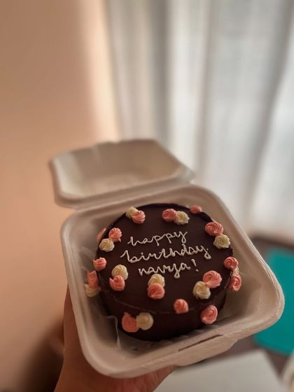 A rich chocolate bento cake decorated with a "Happy Birthday" message and small, piped buttercream flowers in pink and white.