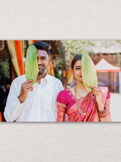 A playful and creative portrait of the bride and groom, each peeking out from behind a large green leaf.