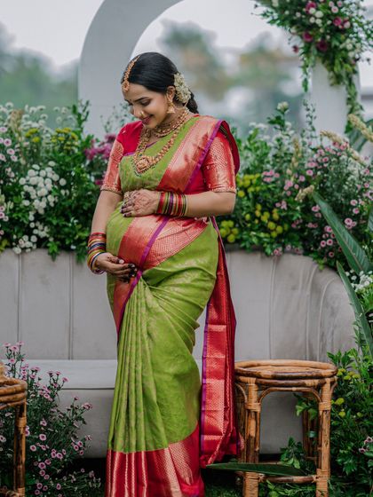 A mother-to-be cradling her baby bump. The saree is draped to highlight this beautiful phase of her life.