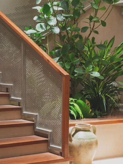 A detailed look at the staircase railing. The design combines a warm wood handrail with a perforated metal screen, a modern detail that allows light to filter through while ensuring safety.