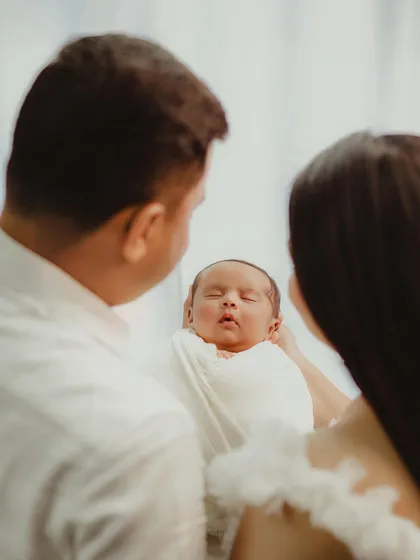 A creative shot from behind the parents, focusing on the precious newborn held between them.