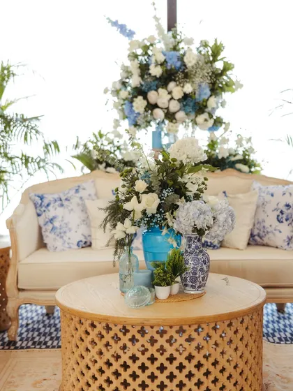 A lounge area with a carved wooden coffee table, chinoiserie-print cushions, and beautiful blue and white floral arrangements, creating a chic and comfortable space.