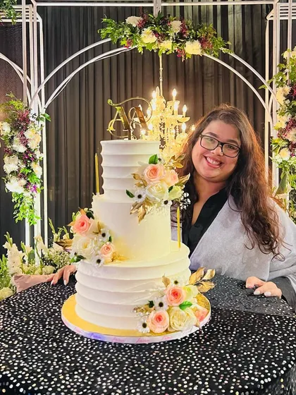 This is my happy place. Posing with this grand, three-tiered wedding cake, decorated with a spiral of buttercream texture and fresh flowers, at the beautifully lit venue.