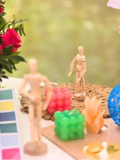 An artfully arranged table with wooden mannequins, colorful candles, and a paint swatch, creating a playful and creative tablescape.