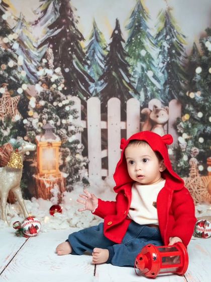 A baby enjoys our winter wonderland Christmas setup, complete with a festive red coat and a snowy forest backdrop.