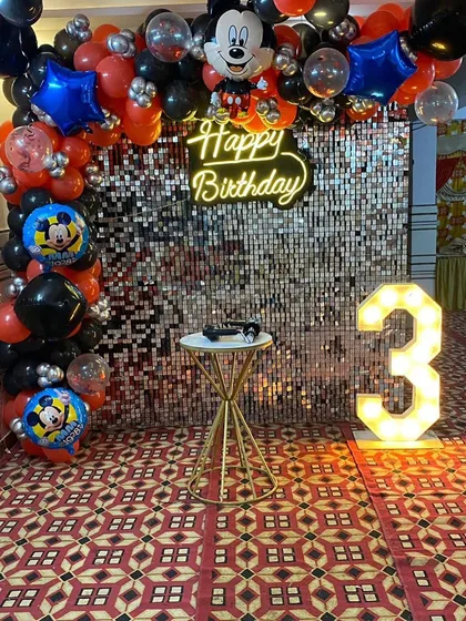 A classic Mickey Mouse theme for a 3rd birthday, featuring a silver shimmer wall, a red and black balloon arch with Mickey Mouse foil balloons, and a light-up number '3'.