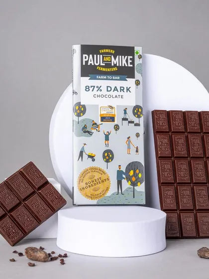 An artistic composition featuring dark chocolate bars on white geometric pedestals. This elevated styling makes the product look like a piece of luxury.