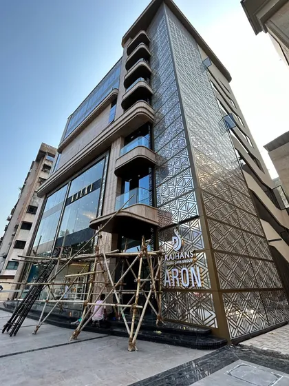 A photograph from a live construction site, showing the facade of a commercial building nearing completion. This image highlights the intricate metal screenwork and the building's strong vertical lines.