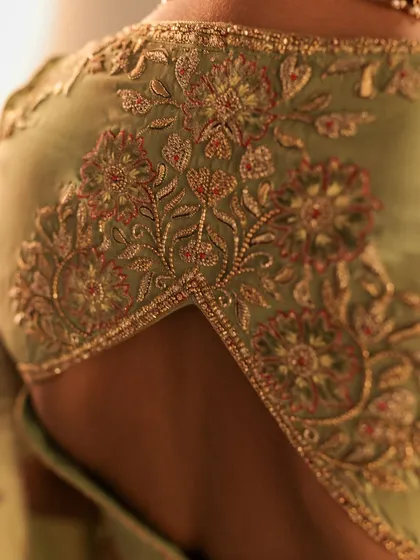 A macro shot of the embroidery on a sage green blouse. This image highlights the fine threadwork and bead detailing that creates a subtle, elegant floral pattern on the back.