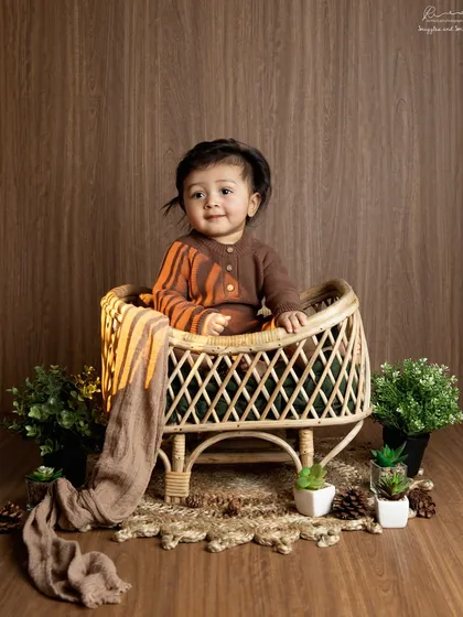 A rustic, woodland-themed setup for a sitter session. This little explorer looks right at home in this cozy cane chair surrounded by greenery.