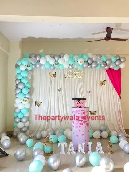 A simple and elegant butterfly theme, perfect for a home celebration. The arch of mint green and silver balloons against a white curtain looks fresh and modern.