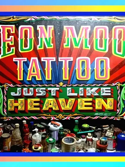 A large, spectacular sign for Neon Moon Tattoo in Kentucky, USA. The piece is full of classic pin-up style figures, a roaring tiger, and bright, explosive lettering that says "Tattoo Just Like Heaven."