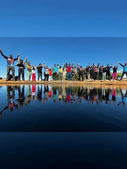 A large group of trekkers celebrating by a stunning mountain lake, their reflection perfectly mirrored in the water. This image captures the incredible sense of community and shared achievement on our treks.
