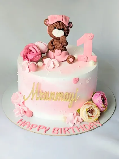A sweet teddy bear cake for a first birthday celebration. This pink cake features a cute bear topper, flowers, and meringues.