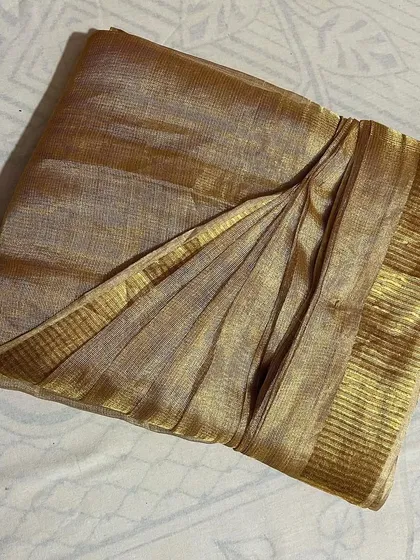 A beautiful tissue silk saree in a muted gold, folded to protect its delicate material.