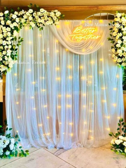 An elegant backdrop with a white floral frame and a 'Better Together' neon sign. The setup is clean, sophisticated, and perfect for Roka ceremonies or anniversaries.