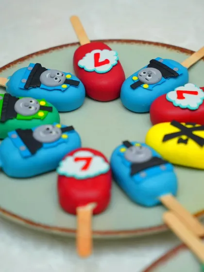 A closer look at the Thomas & Friends themed cakesicles we made for Damian's birthday party. These bite-sized treats are perfect for party favors and are customized to match the main cake, featuring Thomas's face and the birthday number.