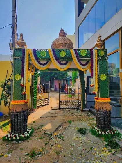 A beautiful and auspicious entrance for a housewarming, featuring a handmade *chappara* with a temple-style dome. The pillars are made of sugarcane, and the entire setup is decorated with fresh marigold flowers.
