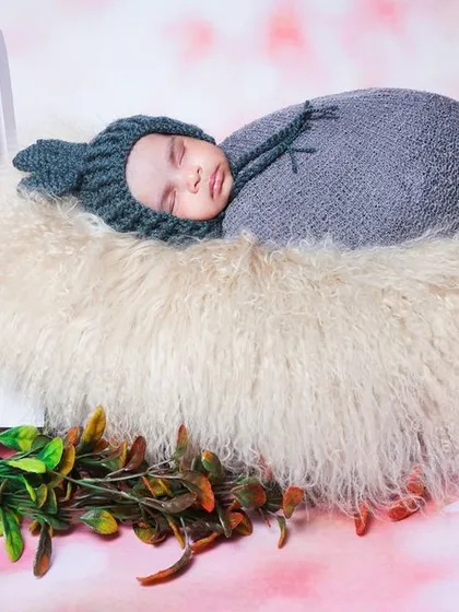 A newborn wearing a cute bunny-eared hat sleeps on a fluffy bed prop. The pink floral background adds a soft, dreamy quality to the image.