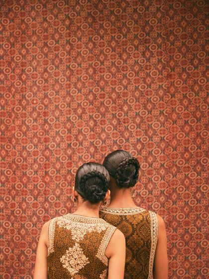 Two models with coordinated hairstyles and outfits against an Ajrakh wall. This image for Anita Dongre is about symmetry, pattern, and the shared heritage of Indian crafts.