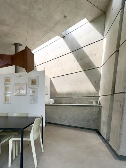 This is the dining area in our 'House of Stories' project, where shafts of natural light cut through the double-height space, transforming the raw concrete walls throughout the day. We designed this home as a sanctuary for a writer, where the interplay of light and shadow creates a quiet, contemplative atmosphere.