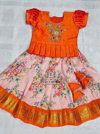 A floral pattu lehenga for newborns and babies. The orange peplum top is paired with a pink floral printed skirt, creating a bright and cheerful look.