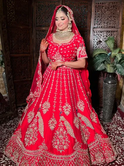 A full view of a beautiful bride in a red lehenga with peacock embroidery. This rental piece offers a designer look that is both stunning and affordable.