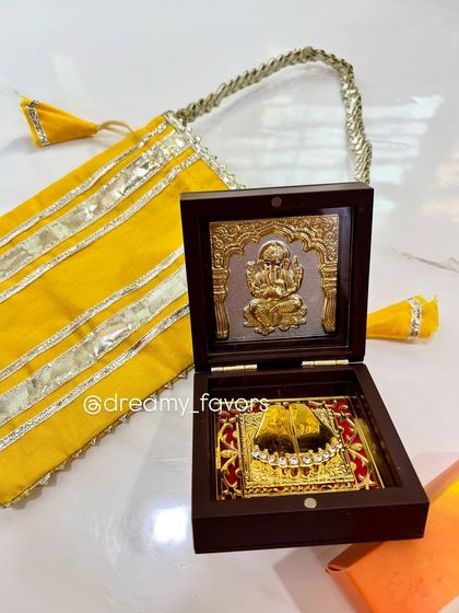 This Ganesh Charan Box is a divine keepsake, featuring a gold-plated charan paduka inside a wooden box. Paired with a traditional yellow potli bag, it serves as a beautiful symbol of blessings and prosperity.