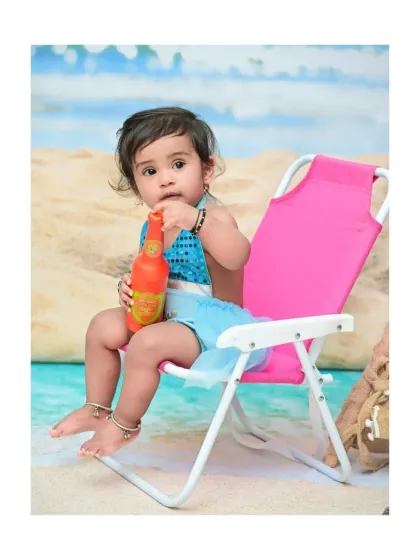 A cute close-up of the baby girl on her pink beach chair, curiously inspecting her toy bottle. These little moments of discovery are what make baby photoshoots so special.